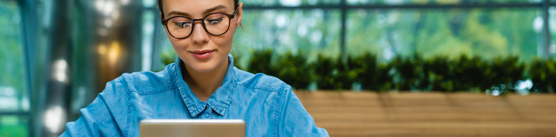 Nice-looking young caucasian businesswoman using tablet at the desk in modern office